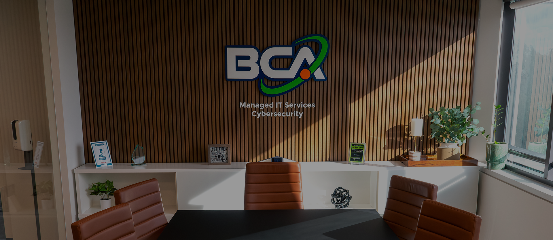 Modern conference room at BCA IT with brown leather chairs around a black table, featuring a wooden accent wall with the BCA logo and the words 