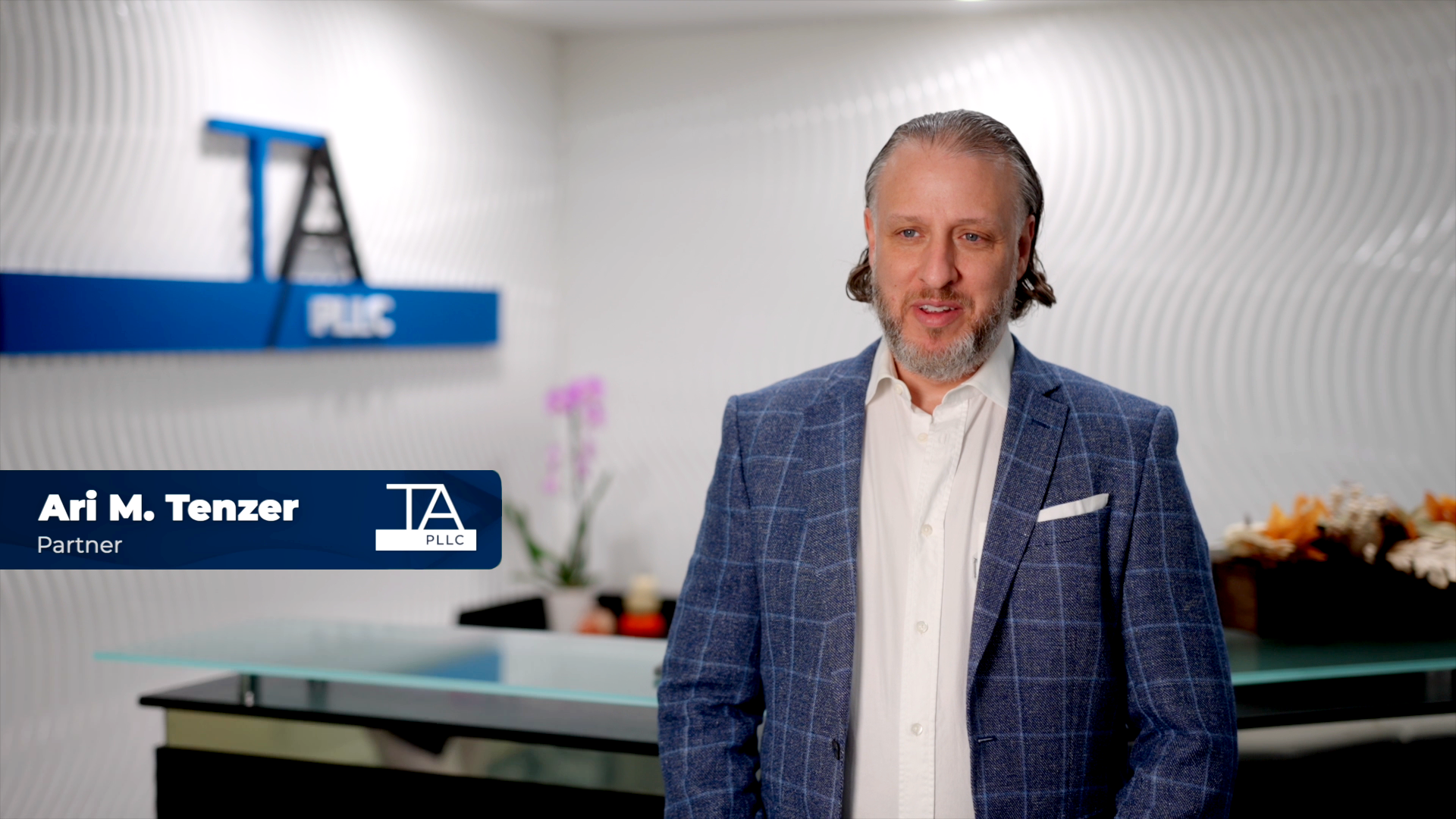 Attorney testimonial video still featuring a partner at TA PLLC law firm, standing in the office lobby with the TA PLLC logo in the background.