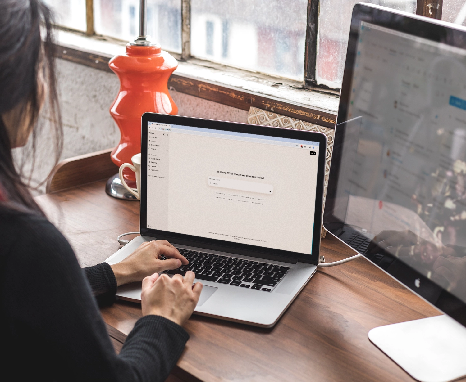 Employee using Microsoft Copilot on a laptop at a desk with a desktop monitor nearby.