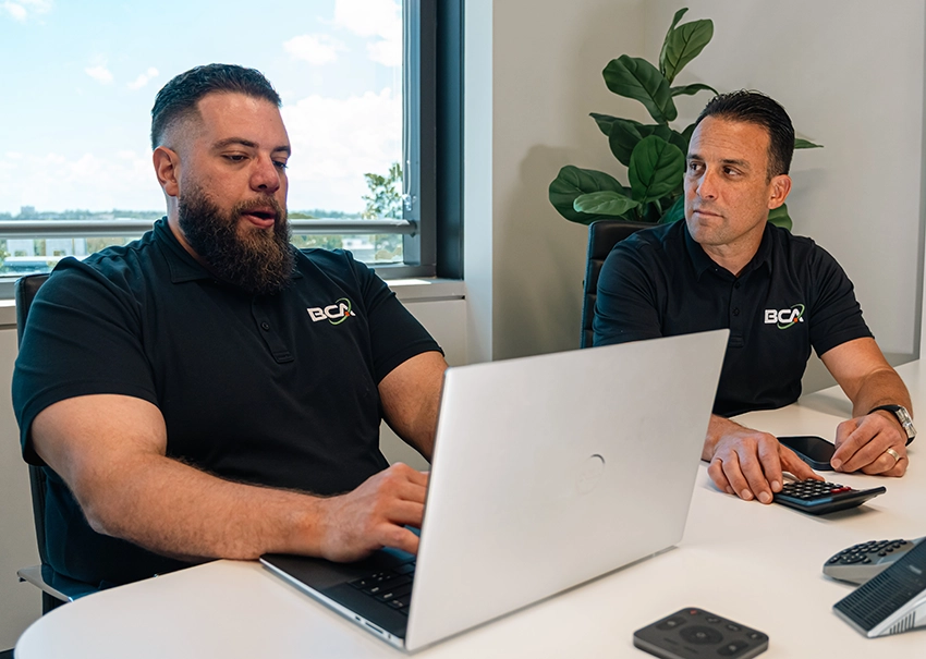 Two BCA IT consultants collaborating on a laptop during a meeting.