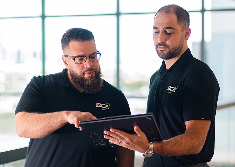 Two BCA IT specialists reviewing project details on a tablet.