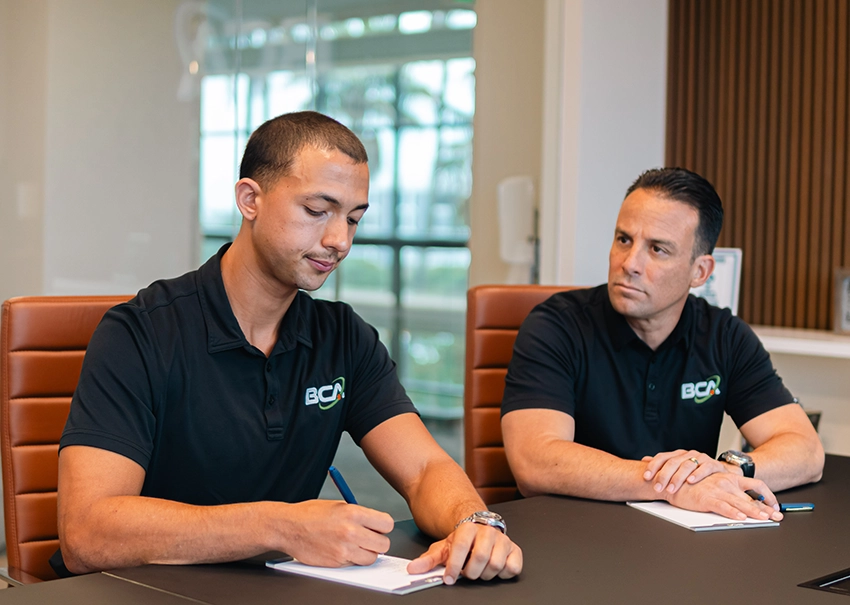 Two BCA IT consultants reviewing and taking notes at a conference table.