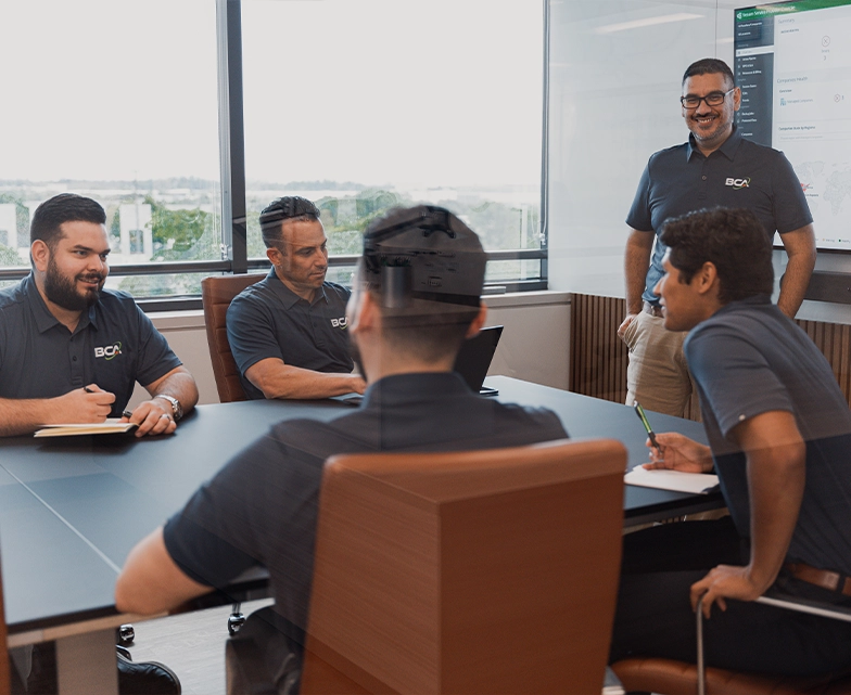 BCA cybersecurity team members gather in a conference room for a meeting, with one team member presenting in front of a screen displaying security software.