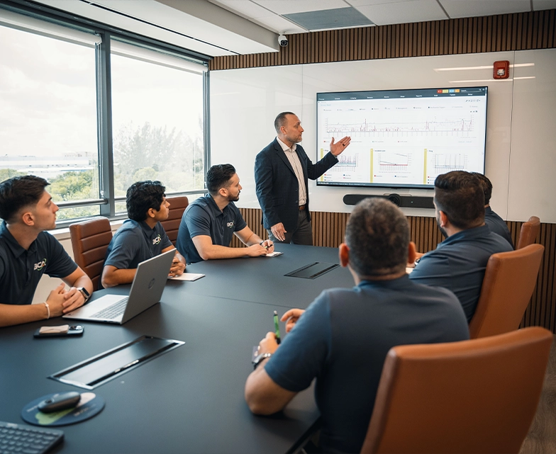 A BCA executive presents cloud services performance data on a large screen during a strategy meeting with the IT team in a modern conference room.