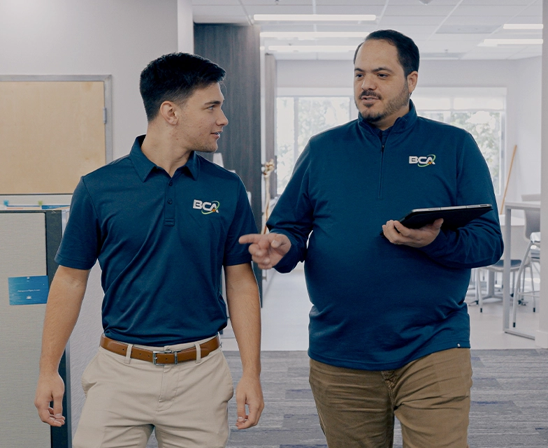 Two BCA team members walking together in the office hallway, discussing work with a tablet.
