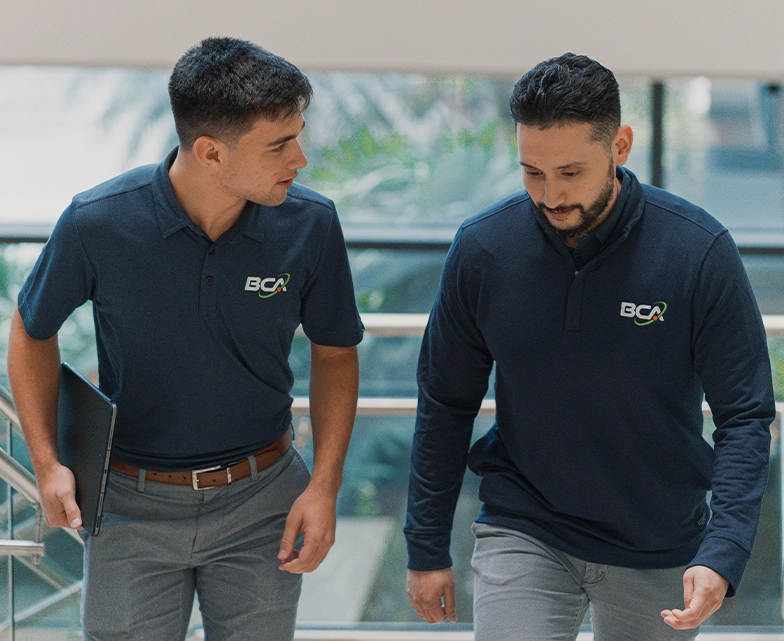 Two BCA team members walking together and discussing work, both wearing branded shirts