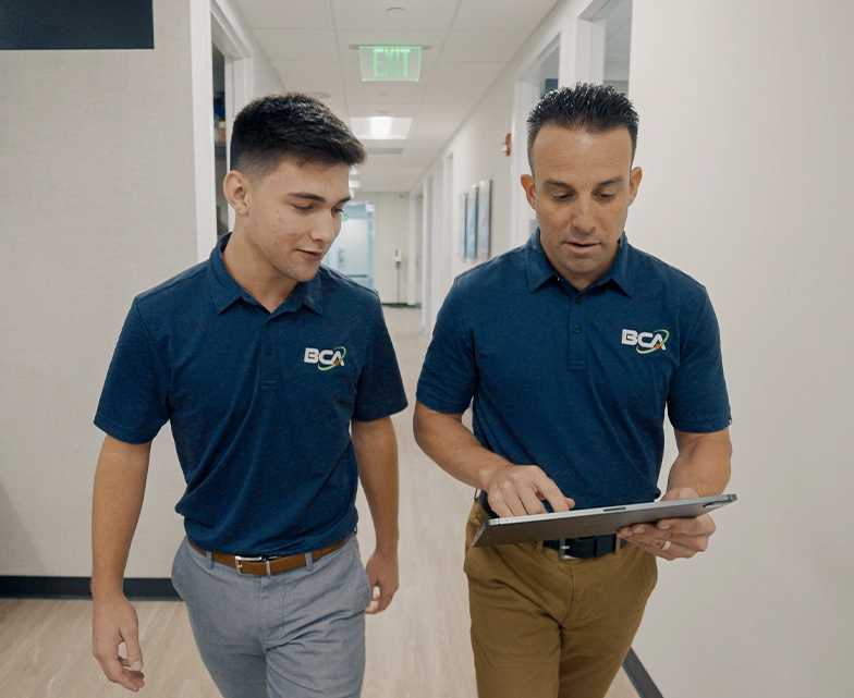 Two BCA team members walking through the office while reviewing information on a tablet.