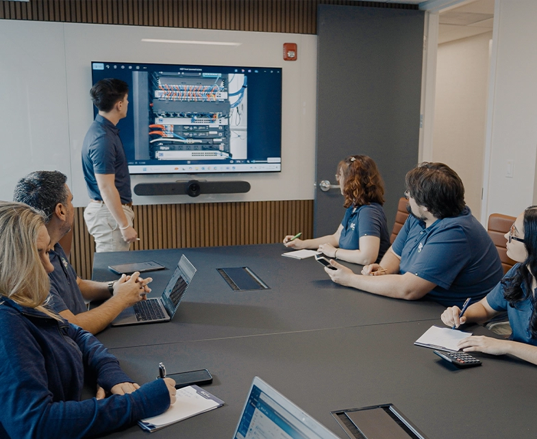 BCA team gathered in a meeting room watching a presentation on a large screen.