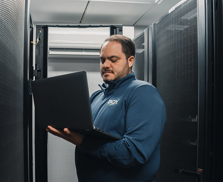BCA technician using a laptop while standing inside a server room.