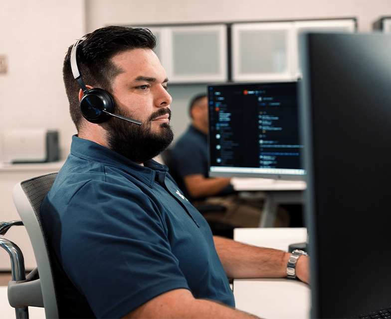 A BCA support specialist wearing a headset focuses on a large monitor, actively assisting a client through a ticketing or communication system.