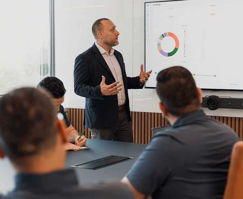 A business professional presents a data dashboard to BCA team members during a strategy meeting, highlighting IT service performance metrics.
